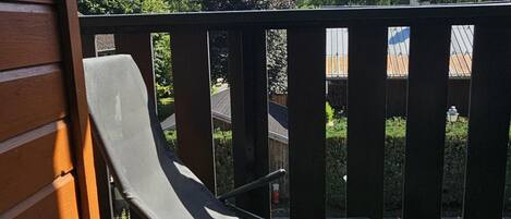 En balkong med ett metallräcke, en fåtölj och utsikt över ett bergskedja och träd.