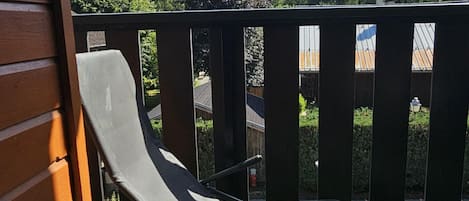 A balcony with a metal railing, a single lounge chair, and a view of a mountain range and trees.