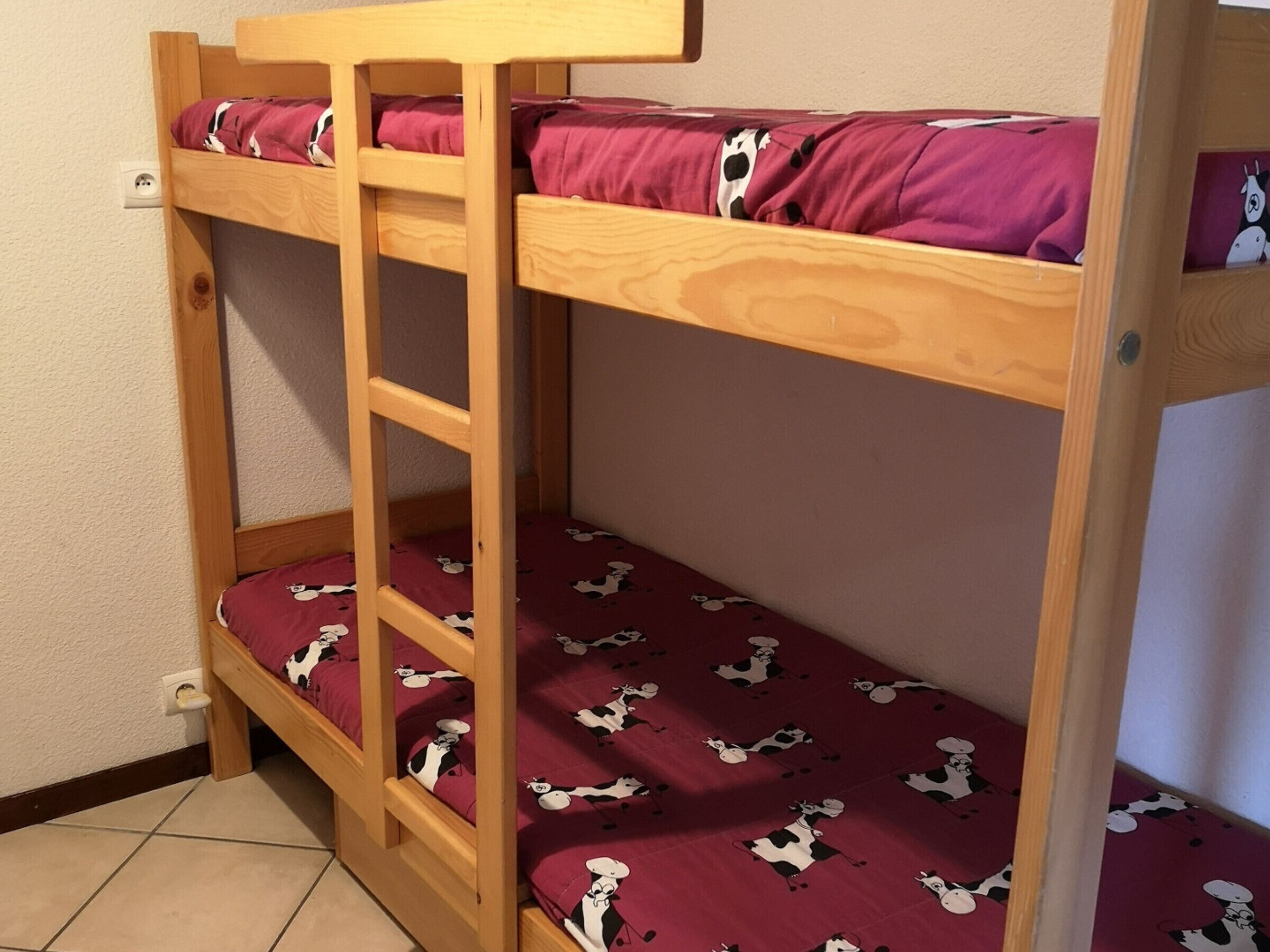 A bunk bed with a ladder, a red mattress with cow patterns, and a wooden headboard.