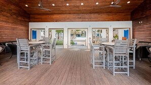 Un vaste espace intérieur aux murs et au plafond en bois, comprenant plusieurs tables et chaises, et offrant une vue sur un espace extérieur grâce à des portes vitrées.