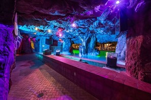An indoor space with a pool, rock formations, and a bar area.