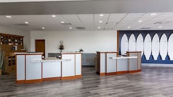 A reception area with two reception desks, a wooden cabinet with various items, and a wall with surfboard decorations.