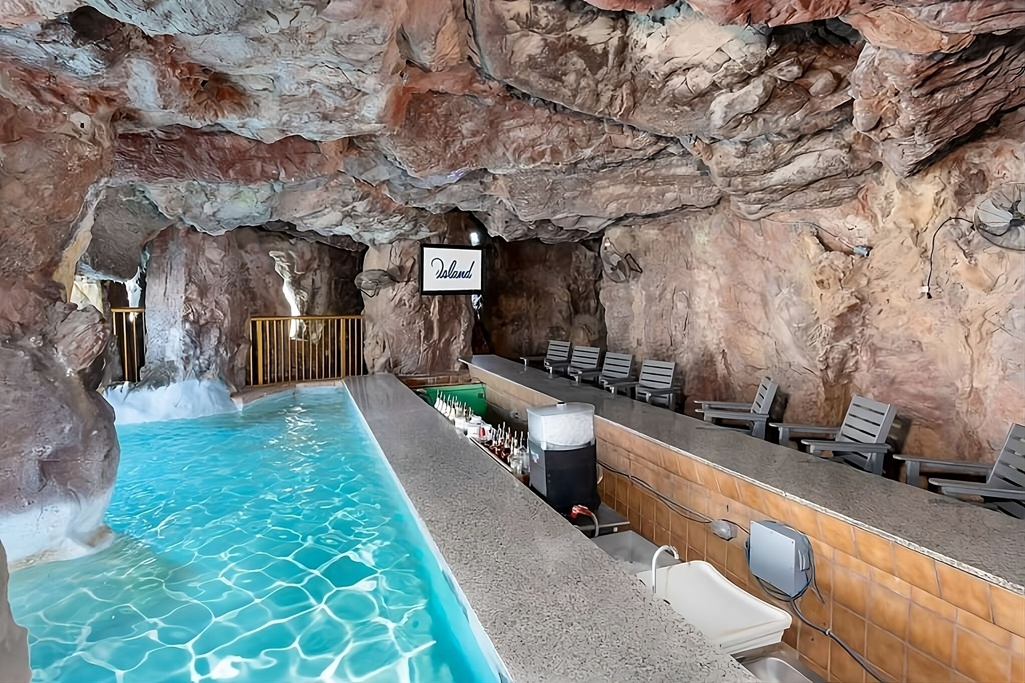 Et poolområde med et skilt med teksten "Island", en bar med siddepladser, og et klippehule-lignende loft.