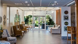 Un hall d’entrée spacieux au design moderne, doté d’une porte vitrée centrale donnant sur un espace extérieur, agrémenté de sièges confortables et d’œuvres d’art décoratives murales.