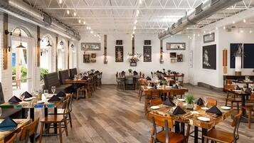 A restaurant with multiple dining areas, wooden furniture, and a white brick wall with framed artwork.