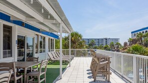 Un balcón de hotel con mobiliario exterior, vista al océano y un edificio con detalles azules al fondo.
