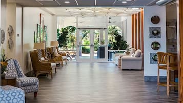 Un lobby espacioso con diseño moderno, que presenta una puerta de cristal central que da a un área exterior, rodeado de asientos cómodos y arte decorativo en las paredes.