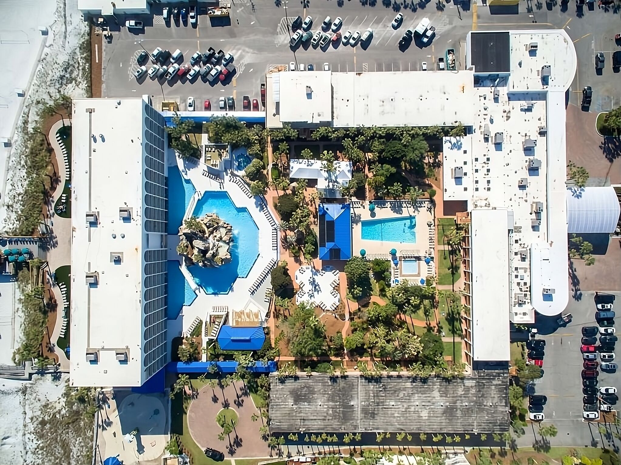 Un edificio grande con un patio central, piscina y zona de estacionamiento.