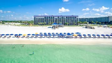 Ein Strandhotel mit einer Reihe von Strandsonnenschirmen und Liegestühlen, freier Sicht auf den Ozean und einem großzügigen Gebäude im modernen Stil.