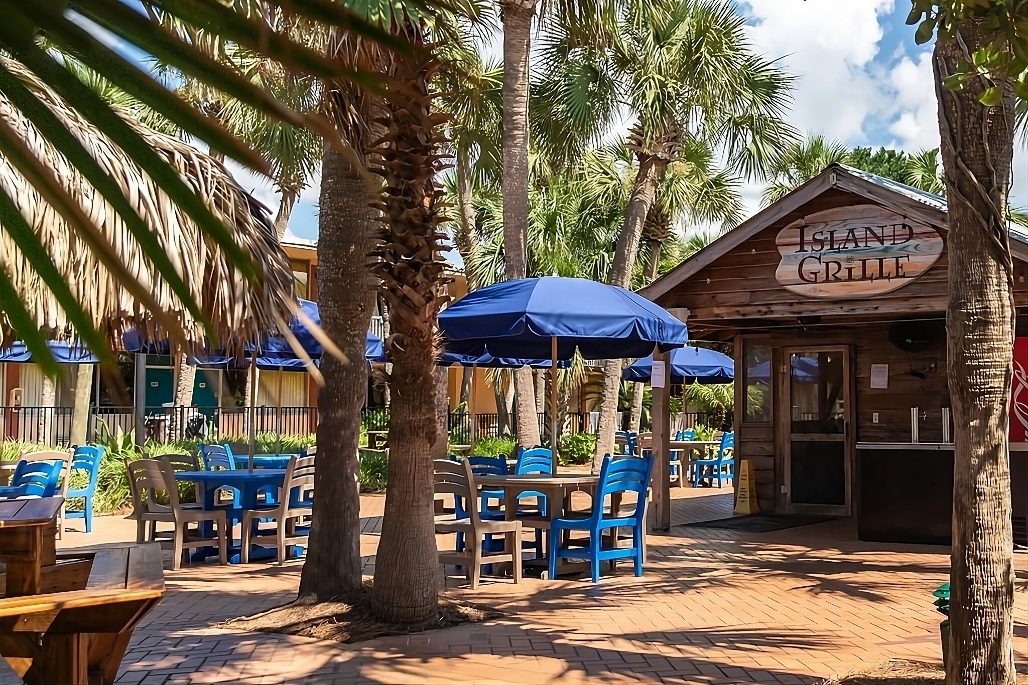 Un restaurante llamado 'Island Grille' con terraza, palmeras y sombrillas azules.