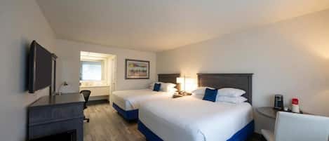 A hotel room with two beds, a desk, a chair, a TV, and a window.