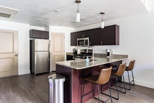 Una cocina moderna con gabinetes oscuros, electrodomésticos de acero inoxidable, encimera de granito y taburetes de bar.