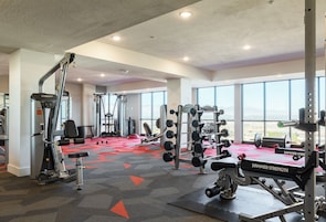 A gym with various exercise equipment, large windows, and a red carpeted floor.
