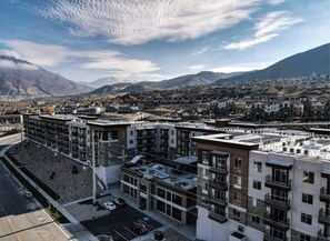 A modern multi-story building with a rooftop terrace, surrounded by a mountainous landscape. - Landing Modern 1bd, Gym (Draper)