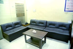A room with a sectional sofa, a small wooden table, and a wall-mounted light switch.
