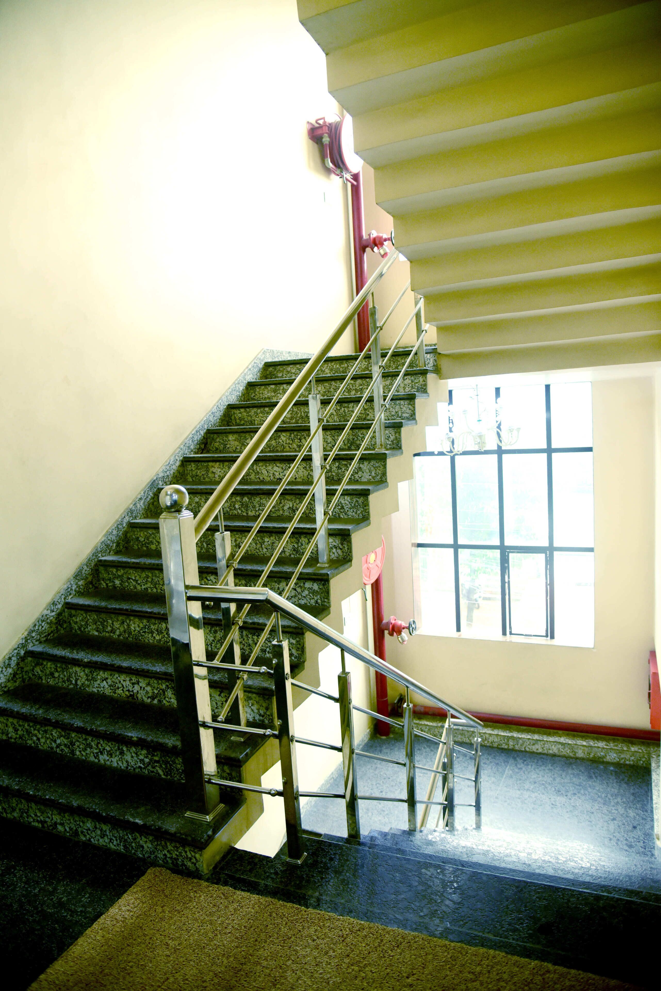 Una escalera con barandales de metal y pasamanos que lleva a un rellano con una ventana.
