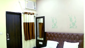 Habitación de hotel con cama, mesita de noche, teléfono, aire acondicionado instalado en la pared, puerta y ventana con cortinas.