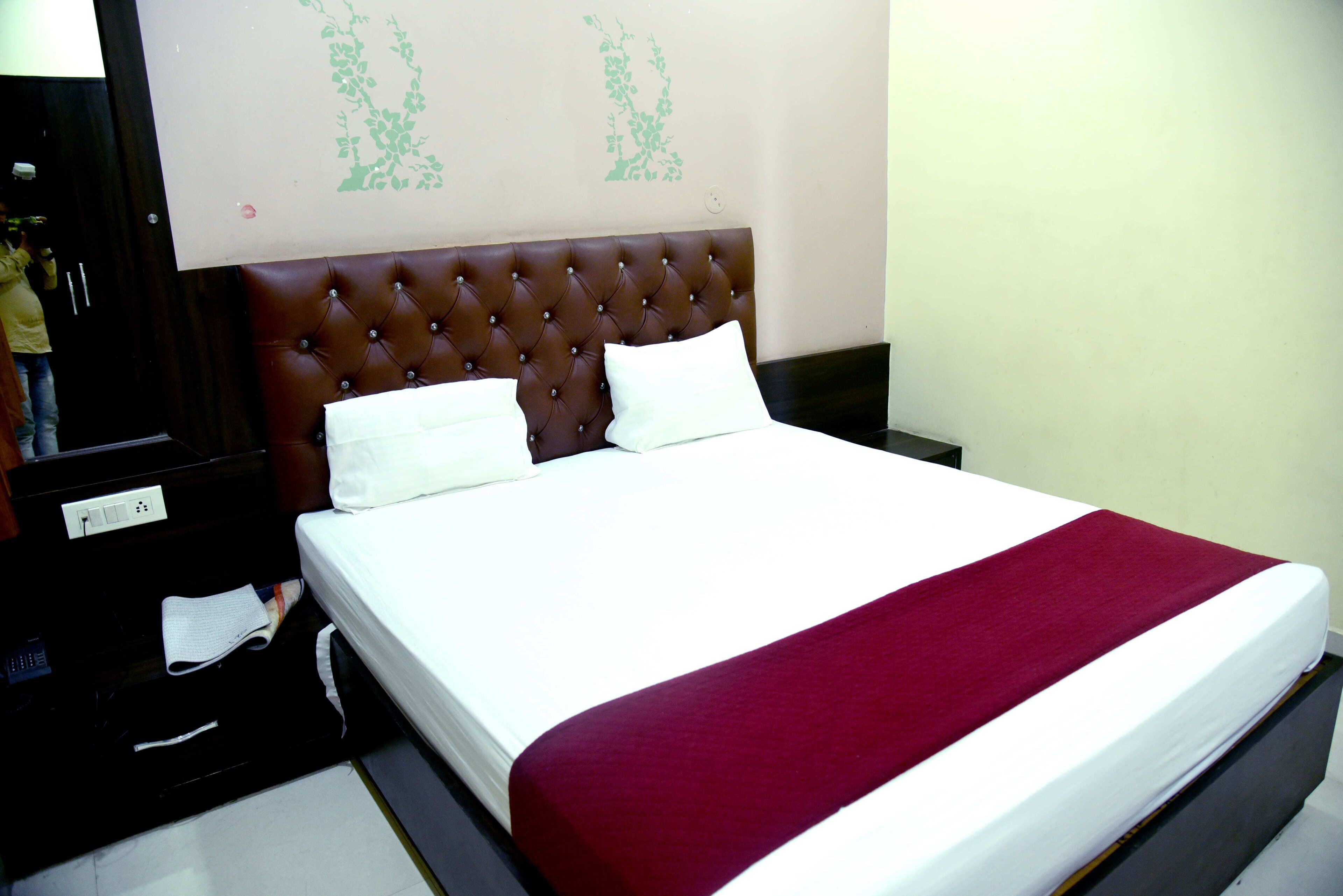 A hotel room with a large bed, a wooden headboard, and a red throw blanket.