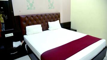 A hotel room with a large bed, a wooden headboard, and a red throw blanket.