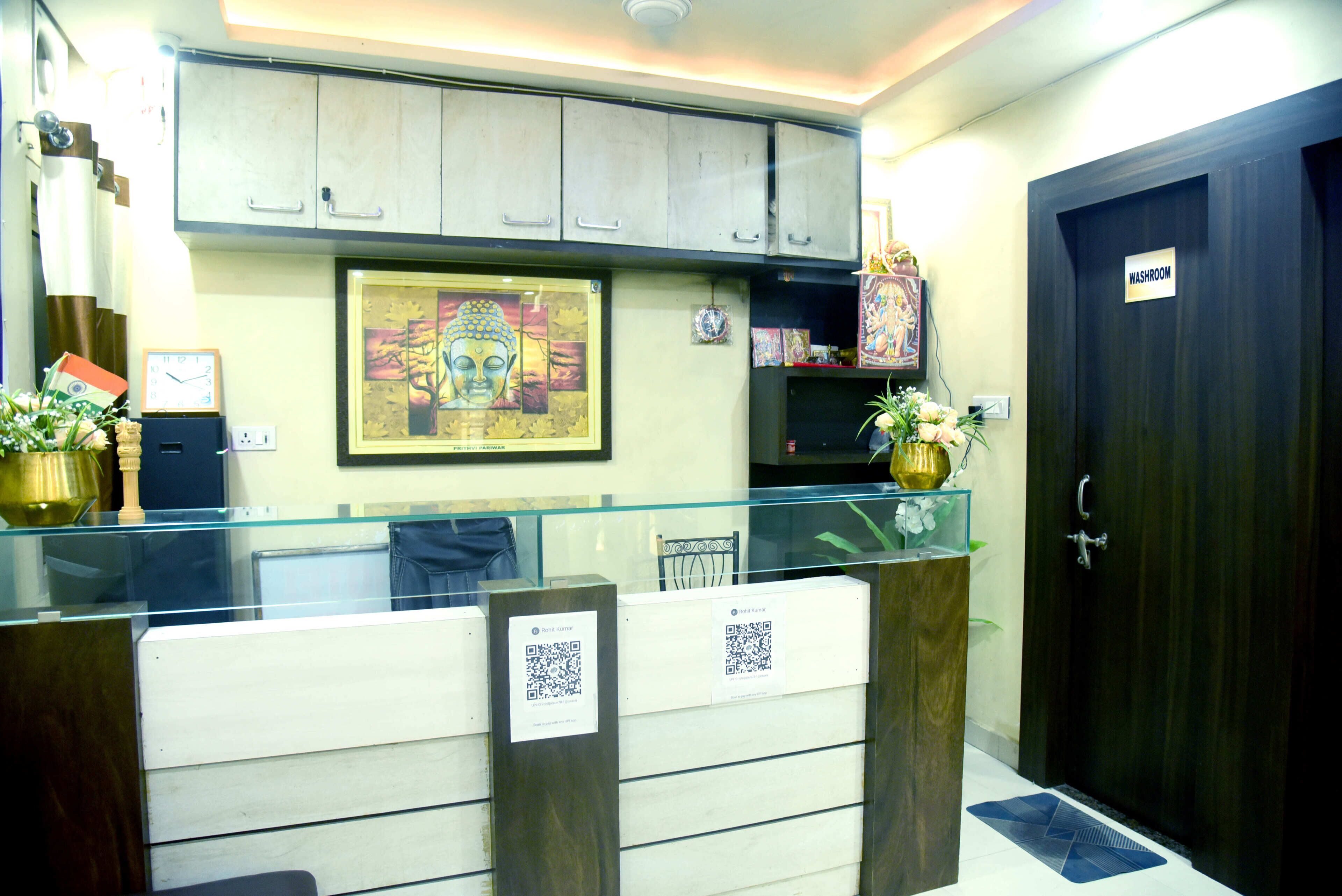 A reception desk with a glass partition, a framed Buddha statue, and a sign indicating a washroom.