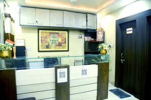 A reception desk with a glass partition, a framed Buddha statue, and a sign indicating a washroom. - MVD Stay by Apex Hospitality (Lucknow)