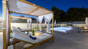 Uma área de relaxamento à beira da piscina, com espreguiçadeiras, uma piscina pequena e uma estrutura de pérgula.