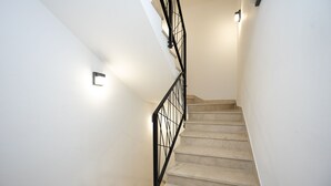 Uma escadaria com corrimão de metal preto e um luminário na parede.