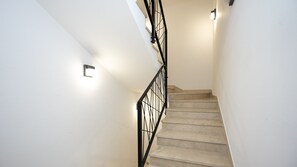 Eine Treppe mit schwarzer Metallreling und einer Wandleuchte.