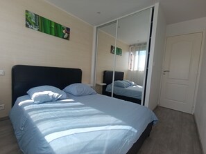 A bedroom with a bed, a mirror, a door, and a wall with a painting. - JULIEN'S 4-ROOM APARTMENT (Tarbes)