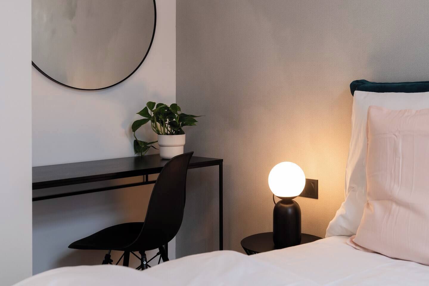 Une chambre d’hôtel avec un lit, un bureau et une chaise, une plante en pot et une lampe de chevet.