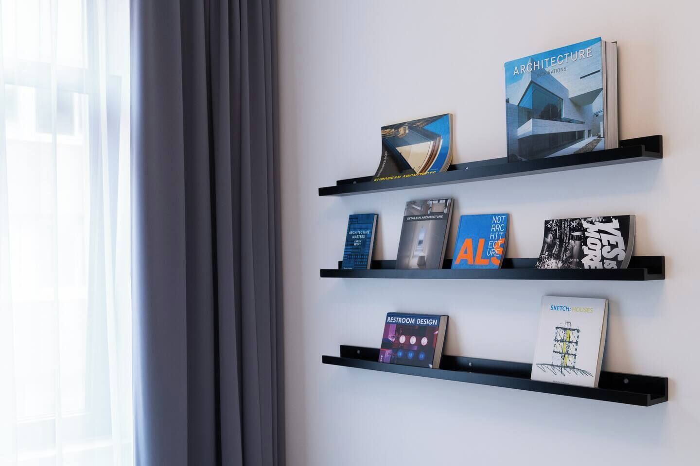 Una pared con tres estantes negros que exhiben libros sobre arquitectura y diseño.