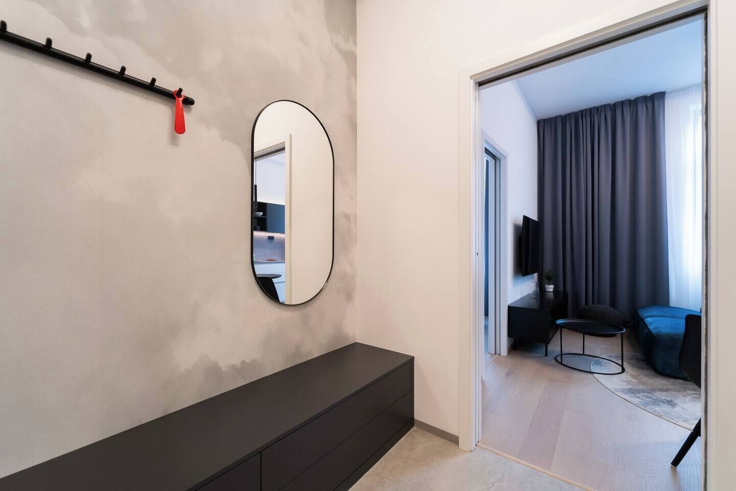 Un intérieur moderne avec une console sombre, un miroir rond et une porte-fenêtre donnant sur un espace de vie équipé d’un téléviseur et de sièges.