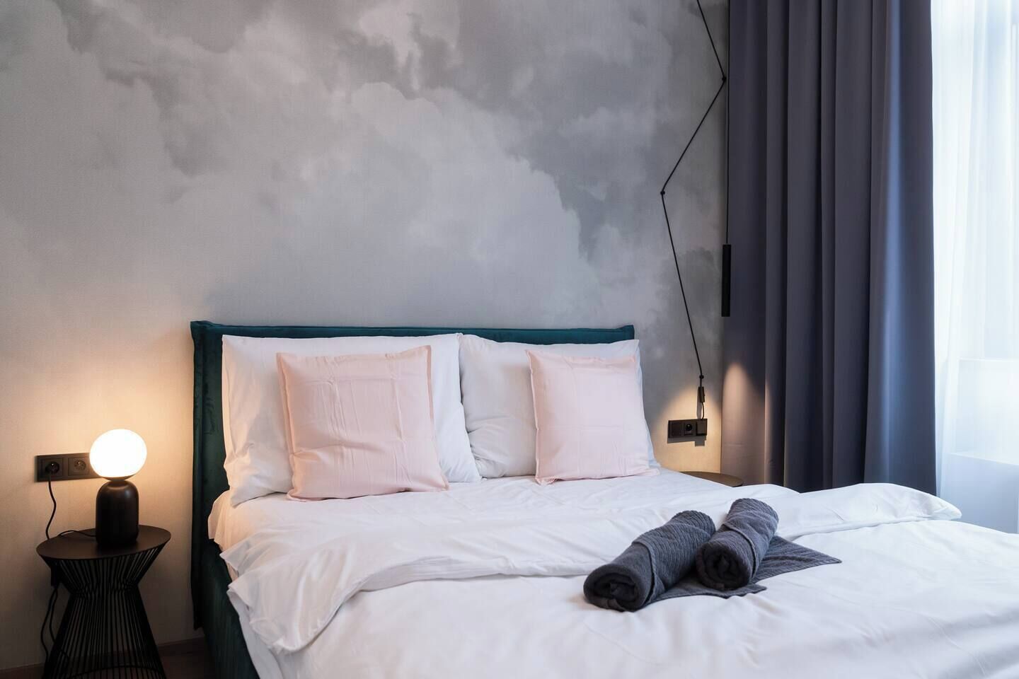 Un letto rifatto con cuscini e un asciugamano arrotolato, una lampada da comodino e una parete con motivo decorativo.