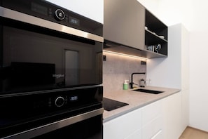Una cocina moderna con microondas integrado, campana extractora de acero inoxidable y encimera con lavamanos.