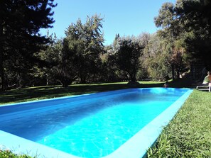 A clear blue swimming pool surrounded by grass and trees.