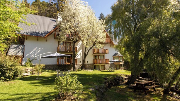 A two-story building with a white exterior, wooden balconies, and outdoor seating areas.