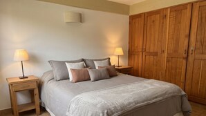 A bedroom with a bed, two bedside tables with lamps, a wooden wardrobe, and a wall-mounted light fixture.