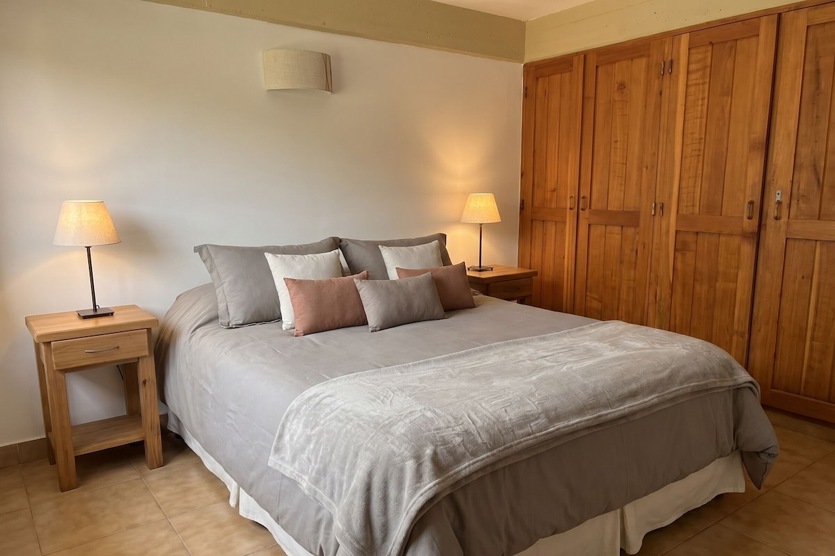 Una camera da letto con un letto, due comodini con lampade, un armadio in legno e un punto luce a parete.