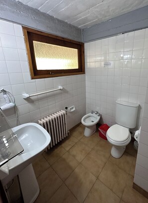 Un baño con inodoro, bidé, radiador y ventana.