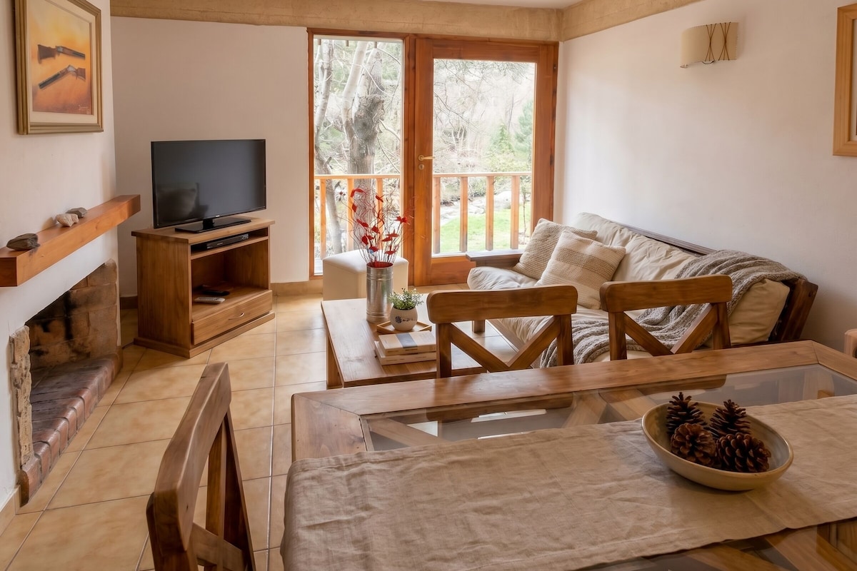 Un soggiorno con televisione, mobili in legno, camino e un balcone con vista sugli alberi.