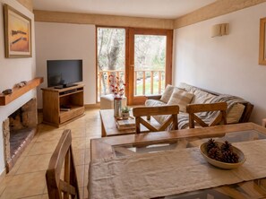 A living room with a TV, wooden furniture, a fireplace, and a balcony with a view of trees.