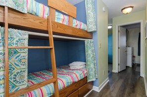 A bunk bed room with a wooden ladder, patterned curtains, and a door leading to another room.