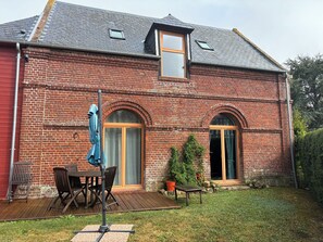 Ein Backsteinhaus mit einer Holzterrasse, zwei Türen und einem kleinen Fenster.