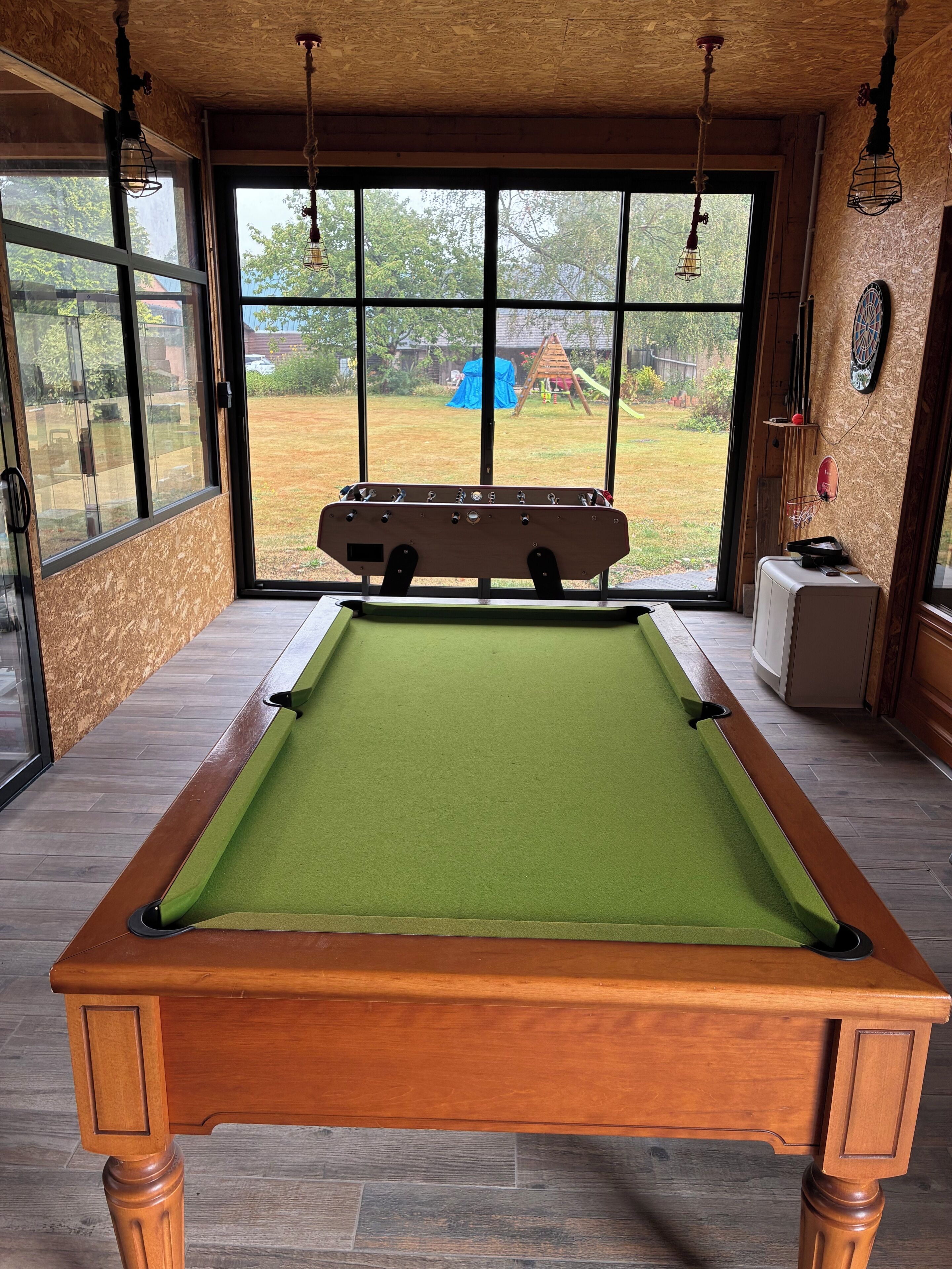 A pool table with a green felt surface, wooden legs, and a wooden table top.