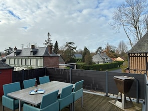 An outdoor patio with a table and chairs, surrounded by a wooden deck and a metal fence. - Renovated Old Norman Stable (Luneray)
