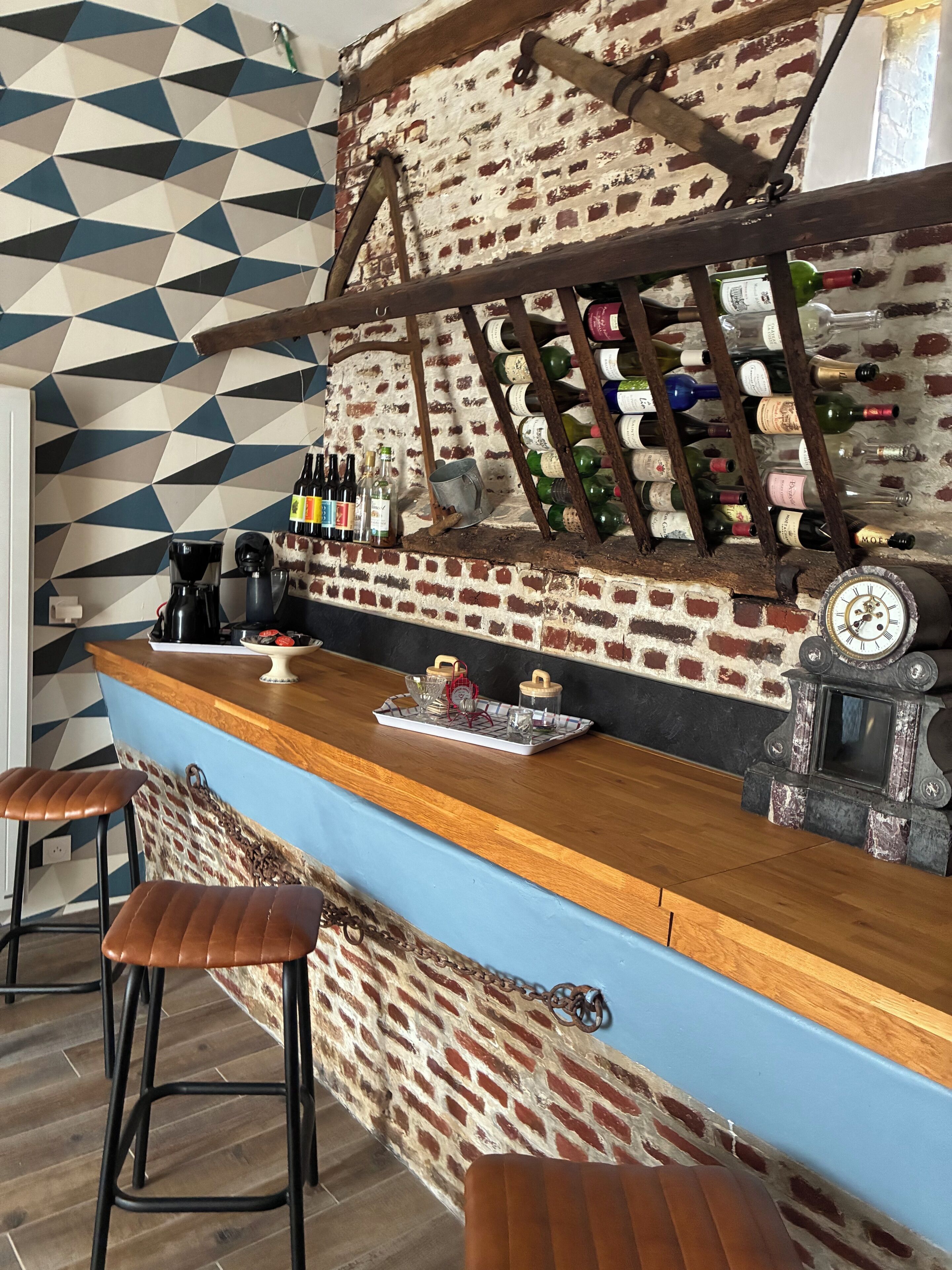 Una zona de bar con pared de ladrillo, botelleros, taburetes y una máquina de café.