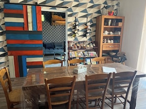 A dining area with a table, chairs, a bookshelf, and a sofa in the background. - Renovated Old Norman Stable (Luneray)