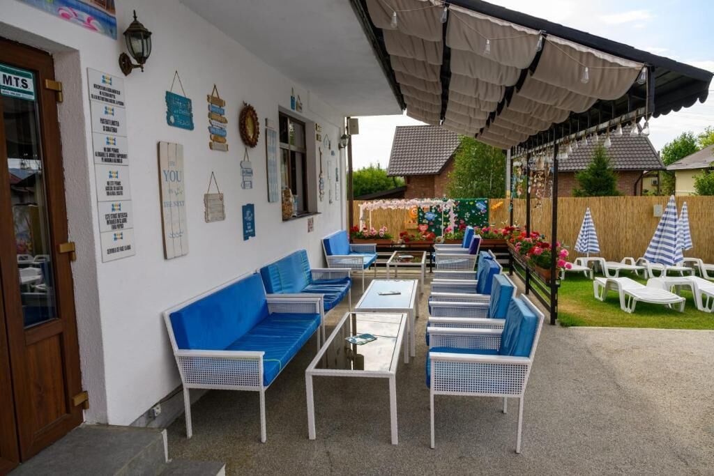 Un espace extérieur aménagé avec des meubles bleus et blancs, une terrasse couverte et un jardin agrémenté de fleurs et d’une clôture.