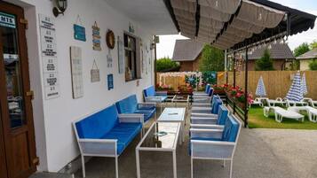 Un espace extérieur aménagé avec des meubles bleus et blancs, une terrasse couverte et un jardin agrémenté de fleurs et d’une clôture.