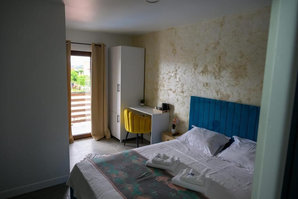 A hotel room with a bed, a desk, a chair, and a view of the outdoors through a door.